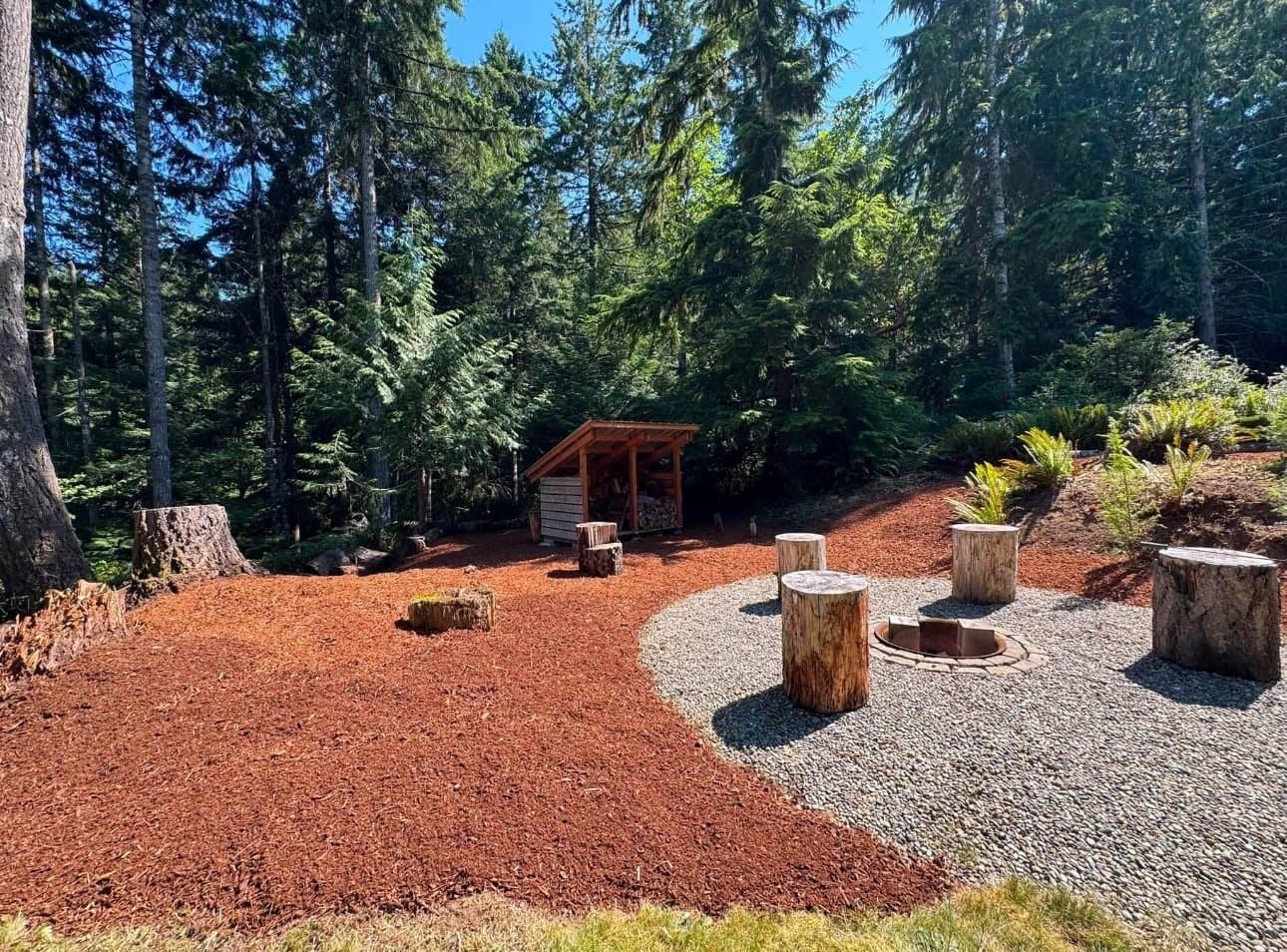Backyard fire pit area with stump seating and bark mulch groundcover